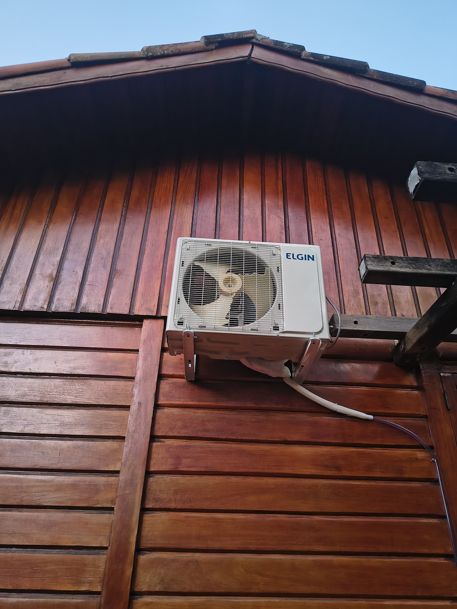 Condensadora Elgin fixada em suporte na fachada de madeira de uma casa