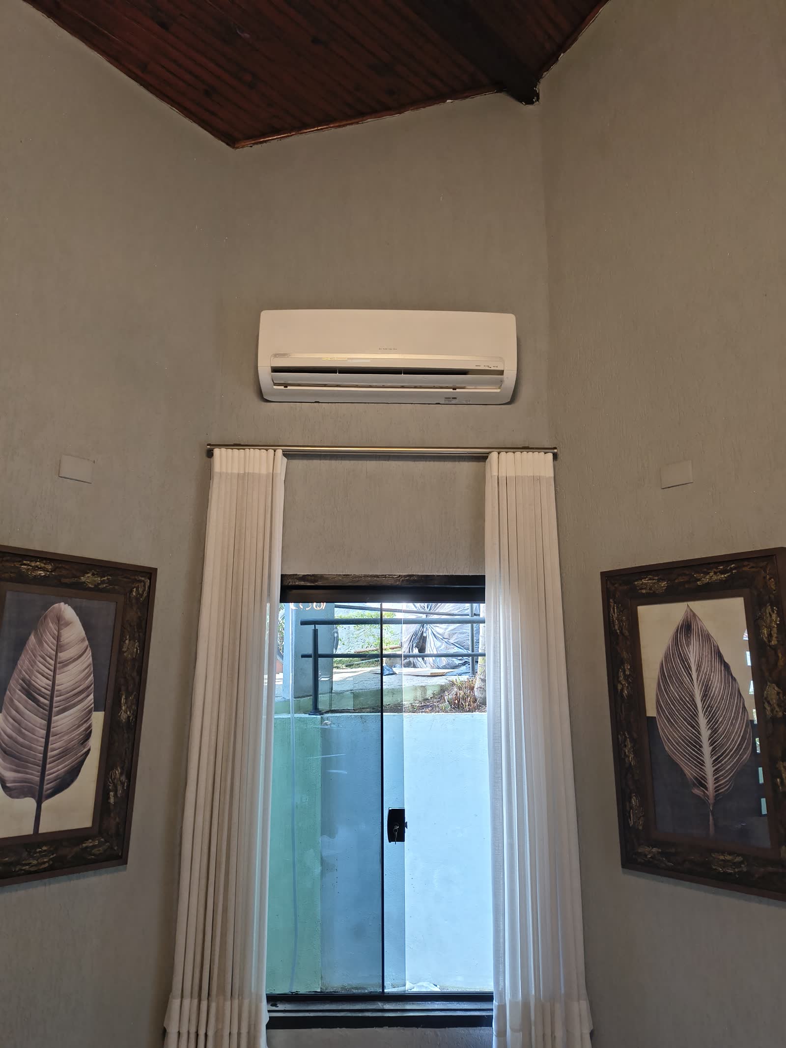 Ar-condicionado split instalado acima da janela de uma sala com cortinas claras e forro de madeira
